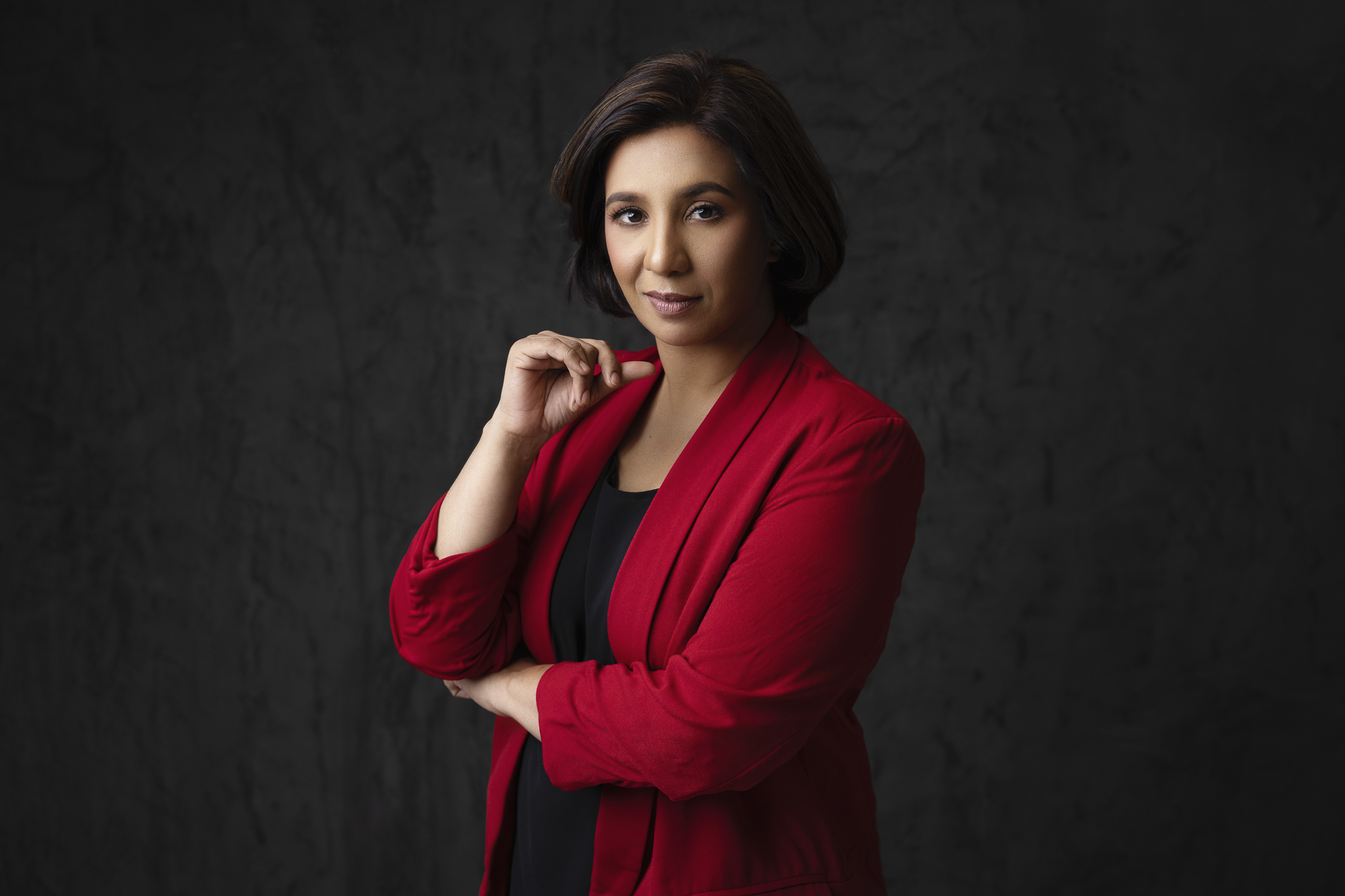 Professional studio business portrait of a woman in red jacket on black backdrop.